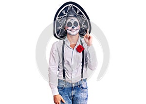 Man wearing day of the dead costume over background showing and pointing up with finger number one while smiling confident and