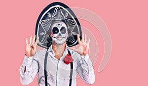 Man wearing day of the dead costume over background showing and pointing up with fingers number nine while smiling confident and