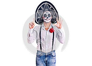 Man wearing day of the dead costume over background showing and pointing up with fingers number six while smiling confident and