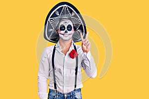 Man wearing day of the dead costume over background showing and pointing up with fingers number two while smiling confident and