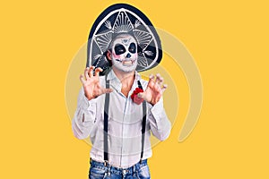 Man wearing day of the dead costume over background smiling funny doing claw gesture as cat, aggressive and sexy expression