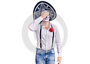 Man wearing day of the dead costume over background smiling and laughing with hand on face covering eyes for surprise