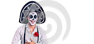 Man wearing day of the dead costume over background smiling and laughing hard out loud because funny crazy joke with hands on body