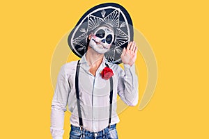 Man wearing day of the dead costume over background waiving saying hello happy and smiling, friendly welcome gesture