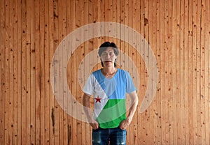 Man wearing Djibouti flag color shirt and standing with two hands in pant pockets on the wooden wall background