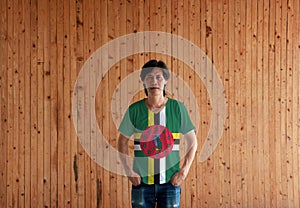 Man wearing Dominica flag color shirt and standing with two hands in pant pockets on the wooden wall background