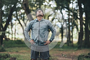 A man wearing earphones and stretching before running. Young man workout before fitness training in the forest. Healthy and