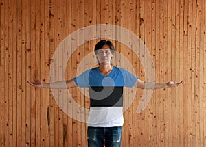 Man wearing Estonia flag color shirt and standing with arms wide open on the wooden wall background