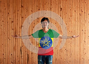 Man wearing Ethiopia flag color shirt and standing with arms wide open on the wooden wall background