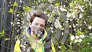 Man wearing face mask decorated with flowers. Man takes off his mask to smell the flowers. Stylish handmade cotton mask