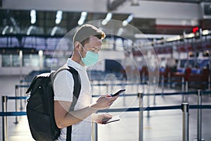 Man wearing face mask and holding smart phone with passport at airport