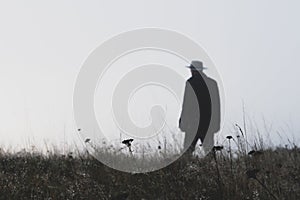 A man wearing a fedora hat standing out of focus on a misty winters day