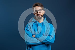 Man wearing glasses and blue hoodie looking disinterested, standing with arms crossed