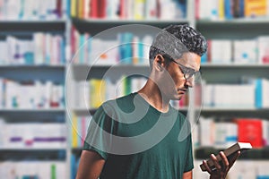 man wearing glasses reading the cover of a book in the library