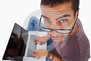 Man wearing glasses sitting on floor using laptop and looking up