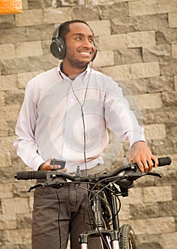 Man wearing grey office pants, white red business shirt standing by bicycle holding mobile phone, headphones on head
