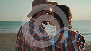 A man wearing a hat and beautiful asian woman kissing on sea beach at sunset. lovely couple travelers in checkered