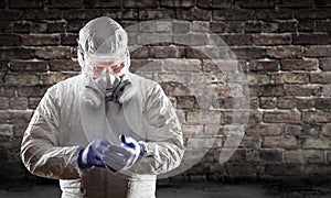 Man Wearing Hazmat Suit, Protective Gas Mask and Goggles Against Brick Wall