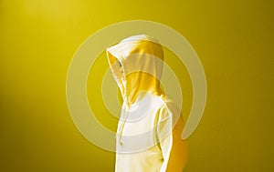 Man wearing hood hidden his face with yellow wall background.