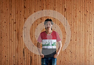 Man wearing Iraq flag color shirt and standing with two hands in pant pockets on the wooden wall background