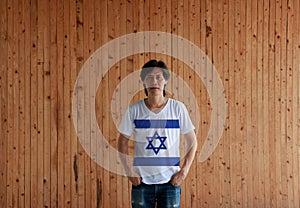 Man wearing Israel flag color shirt and standing with two hands in pant pockets on the wooden wall background