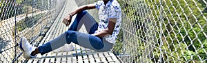 Man wearing jeans sitting around a foot over bridge