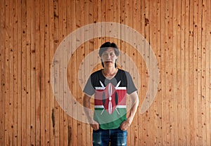 Man wearing Kenya flag color shirt and standing with two hands in pant pockets on the wooden wall background