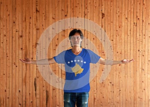 Man wearing Kosovo flag color shirt and standing with arms wide open on the wooden wall background