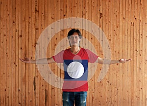 Man wearing Laos flag color shirt and standing with arms wide open on the wooden wall background