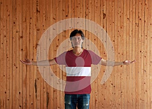 Man wearing Latvia flag color shirt and standing with arms wide open on the wooden wall background