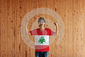 Man wearing Lebanon flag color of shirt and standing with raised both fist on the wooden wall background