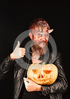 Man wearing makeup holds pumpkin on black background. Devil or monster with October decorations. Halloween party concept