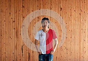 Man wearing Malta flag color shirt and standing with two hands in pant pockets on the wooden wall background