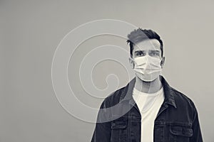 Man wearing medical face mask on light background, space for text. Black and white photography