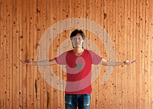 Man wearing Morocco flag color shirt and standing with arms wide open on the wooden wall background