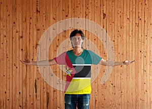 Man wearing Mozambique flag color shirt and standing with arms wide open on the wooden wall background