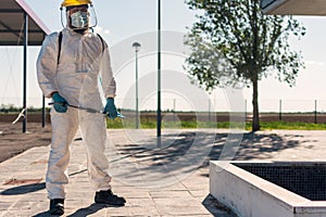 Man wearing an NBC personal protective equipment ppe suit, gloves, mask, and face shield, cleaning the streets with a backpack