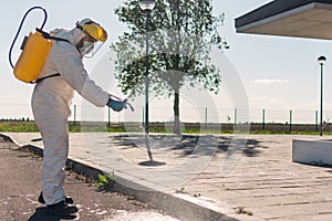 Man wearing an NBC personal protective equipment ppe suit, gloves, mask, and face shield, cleaning the streets with a backpack