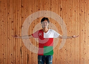 Man wearing Oman flag color shirt and standing with arms wide open on the wooden wall background