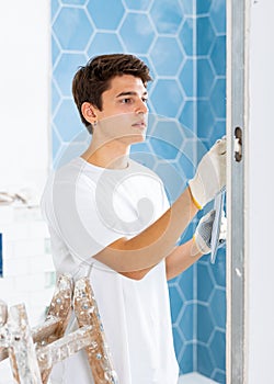 Man wearing ordinary clothes installing ceramic tiles whith construction trowel finish of repairable bathroom