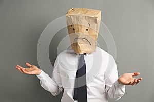 Man wearing paper bag with drawn sad face on grey background