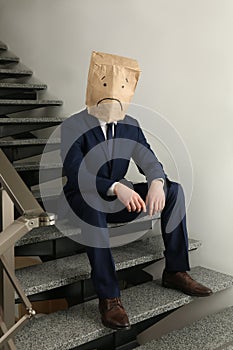 Man wearing paper bag with drawn sad face indoors