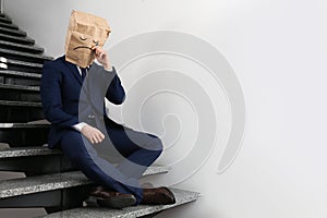 Man wearing paper bag with drawn sad face indoors. Space for text