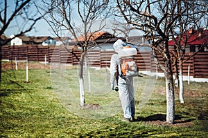 Man wearing protective clothing and spraying insecticide  in fruit orchard