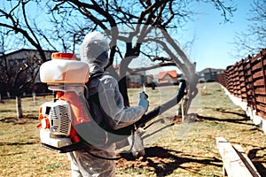 Man wearing protective clothing and spraying insecticide in fruit orchard