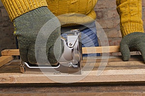 Man wearing protective gloves and using staple gun, fixing wooden objects