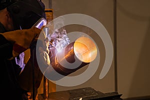 A man wearing a protective mask welds a metal pipe.