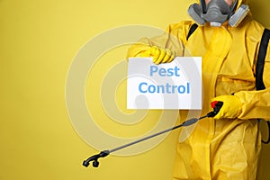 Man wearing protective suit with insecticide sprayer holding sign PEST CONTROL on yellow background, closeup. Space for text