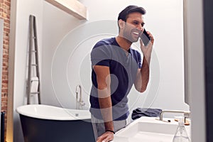 Man Wearing Pyjamas At Home Talking On Mobile Phone In Modern Bathroom