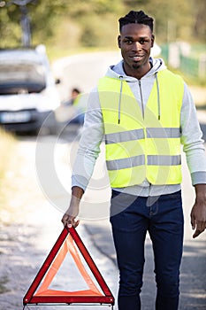 man wearing reflective vest places warning triangle behind breakdown vehicle